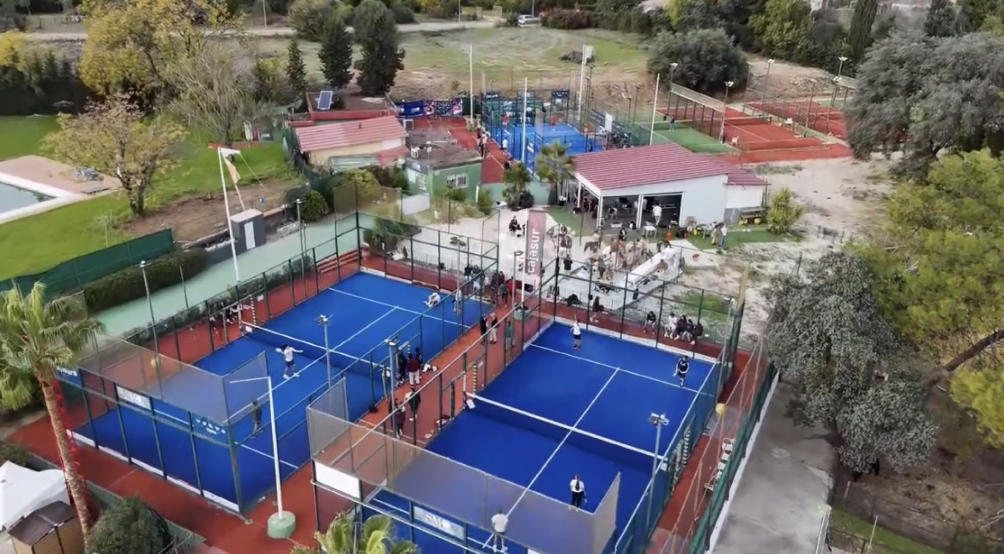 Vista aérea de las pistas de pádel y el campo de fútbol del club, rodeados de pinos